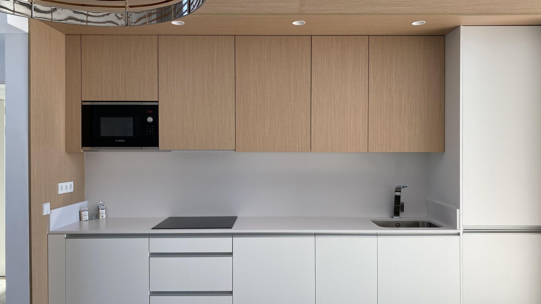 Una cocina con gabinetes blancos, gabinetes de madera, un fregadero y un microondas.