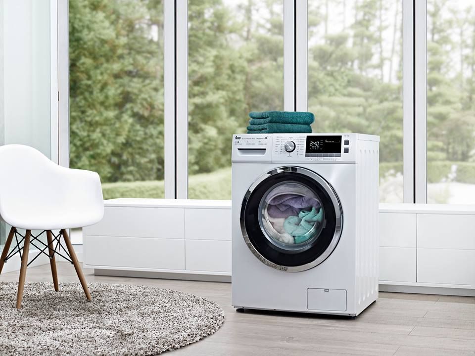 Una lavadora está en una sala de estar al lado de una ventana.