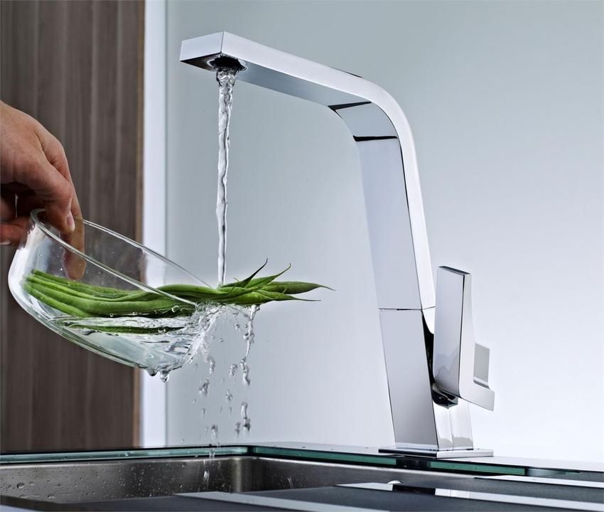 Una persona está lavando judías verdes en un recipiente bajo un grifo.