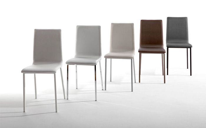 Una fila de sillas de diferentes colores están alineadas en fila sobre una superficie blanca.