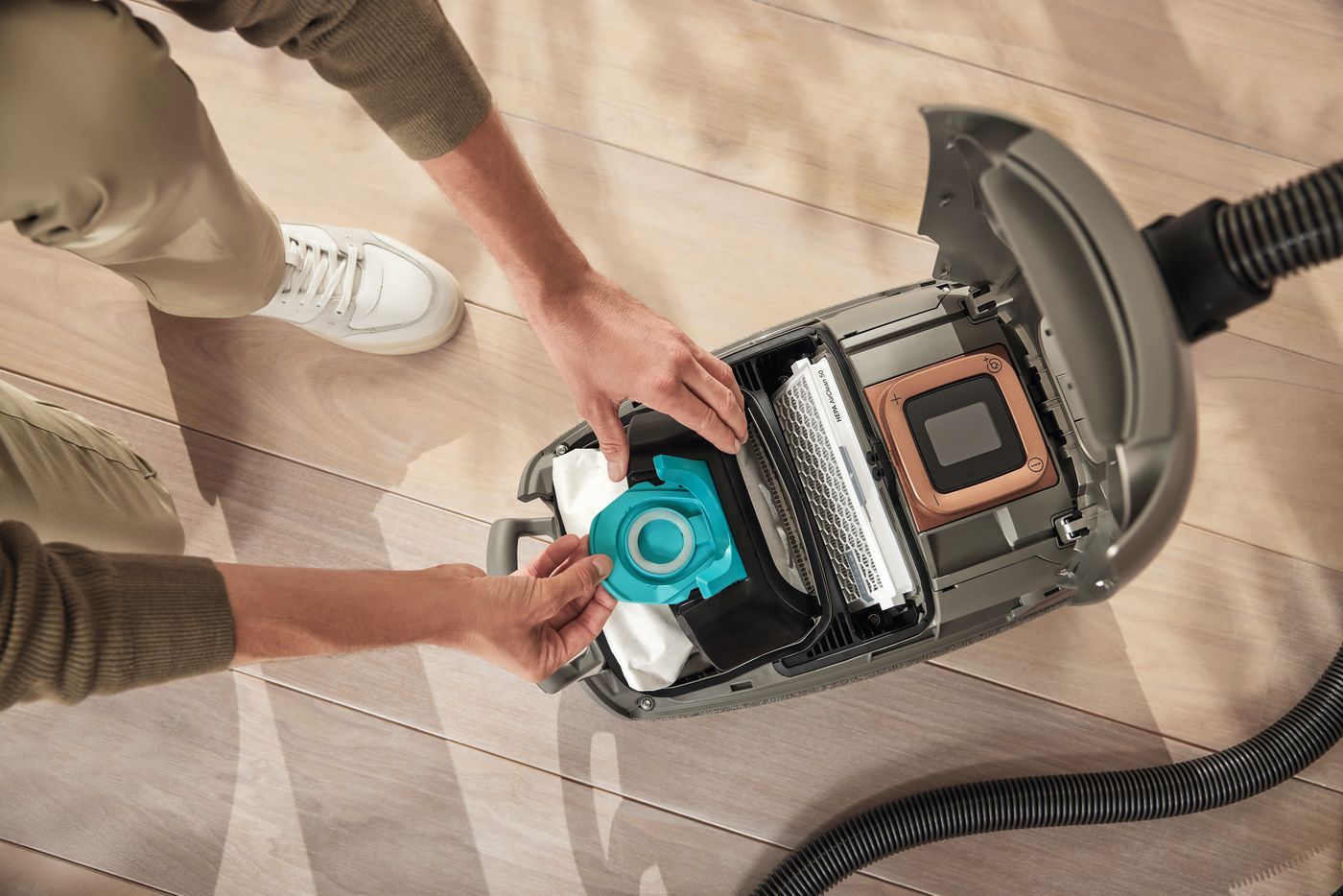 Personne remplaçant le filtre d'un aspirateur sur un plancher en bois.