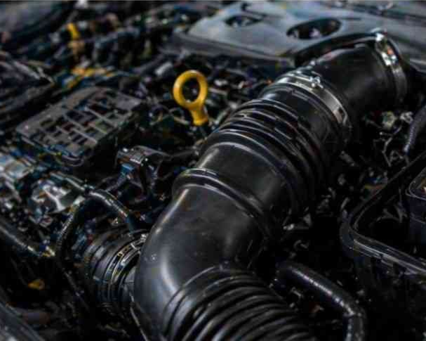 Primer plano del compartimento del motor de un coche con mangueras negras y una varilla medidora de aceite amarilla.