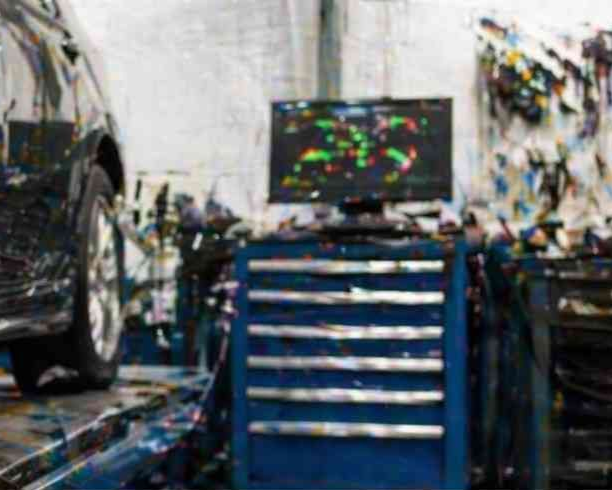 Taller mecánico con una caja de herramientas azul y un coche a la izquierda, visto en el interior borroso de un garaje.