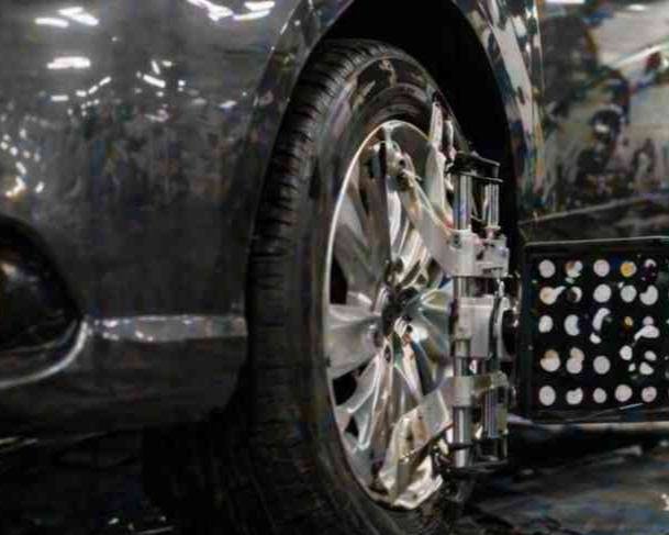 Primer plano de la rueda trasera y la llanta cromada de un coche oscuro en un entorno húmedo y reflectante.