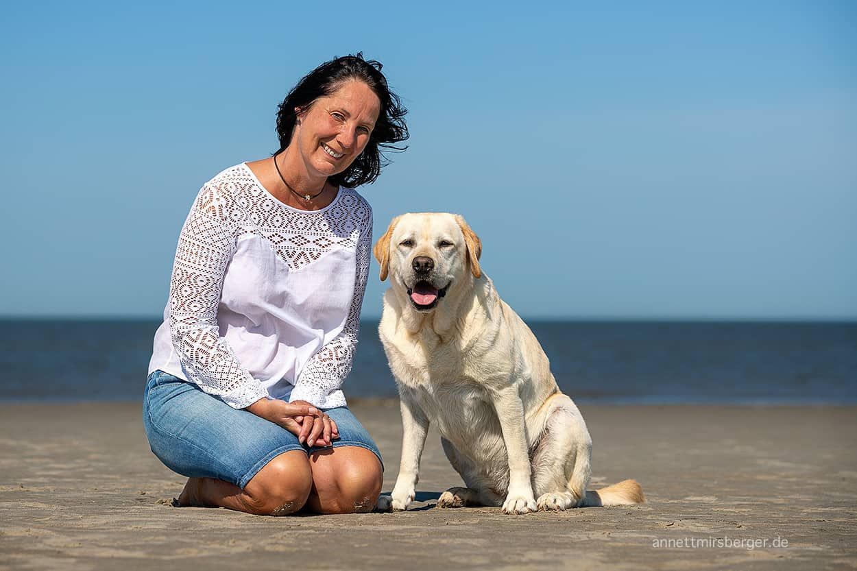 Petra Gassert kniet neben einem Hund am Strand.