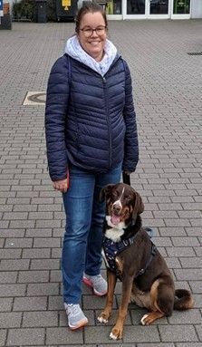 Eine Frau steht neben einem braun-weißen Hund auf einem gepflasterten Gehweg.