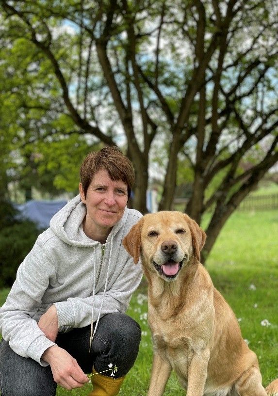 Eine Frau kniet neben einem Hund auf einem Feld.
