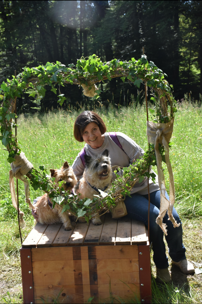 Eine Frau sitzt mit zwei Hunden auf einer Holzkiste.