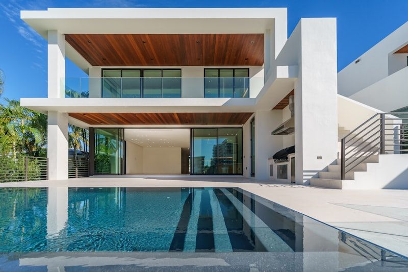 Modern white luxury house with large windows and a swimming pool under a blue sky