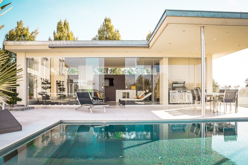 Modern patio with a turquoise swimming pool, outdoor lounge chairs, and a covered terrace by a contemporary house
