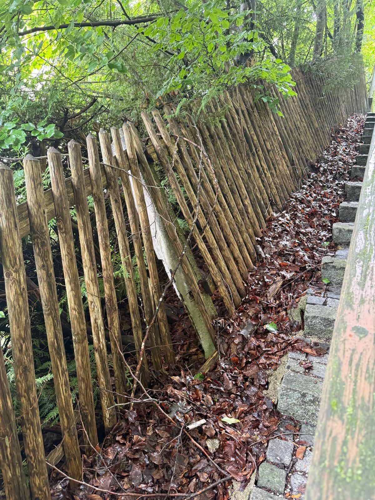 Langer Holzzaun entlang eines bewachsenen Hangs.