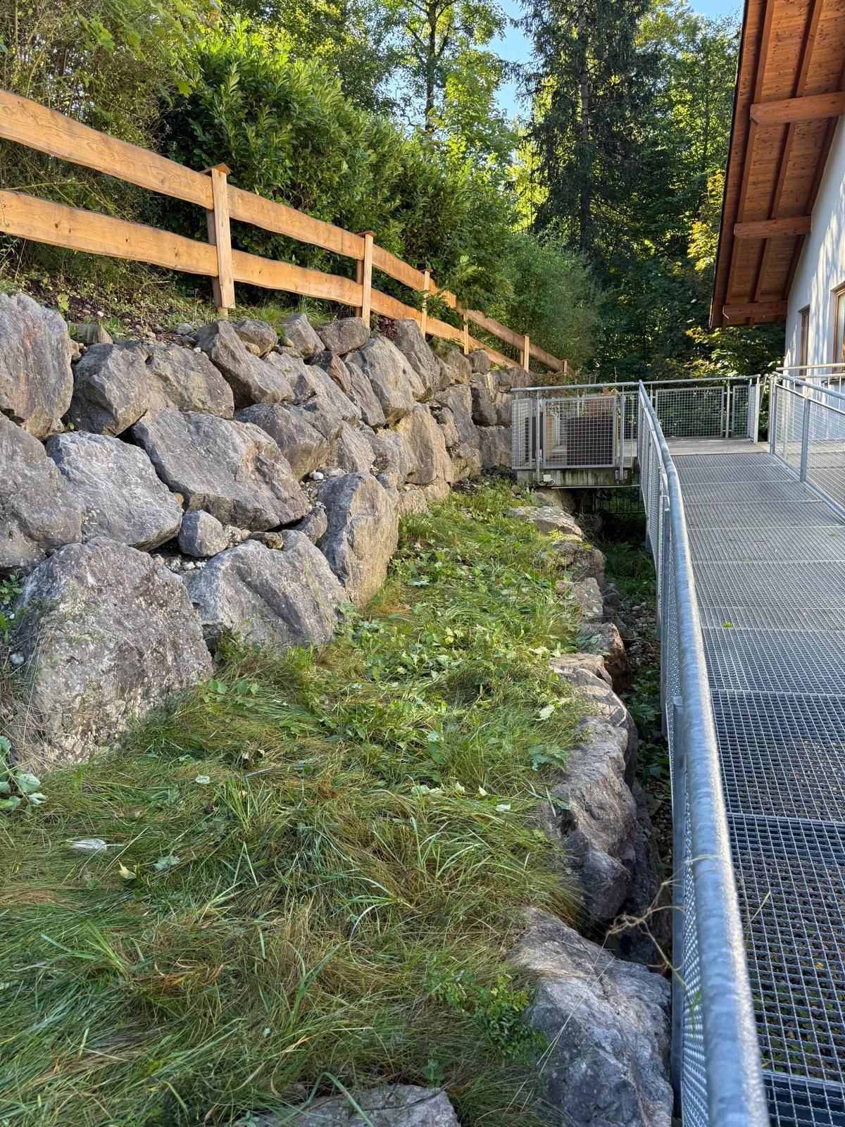 Treppengeländer an einem Grünstreifen der im Hintergrund von einer Steinmauer umgeben ist.