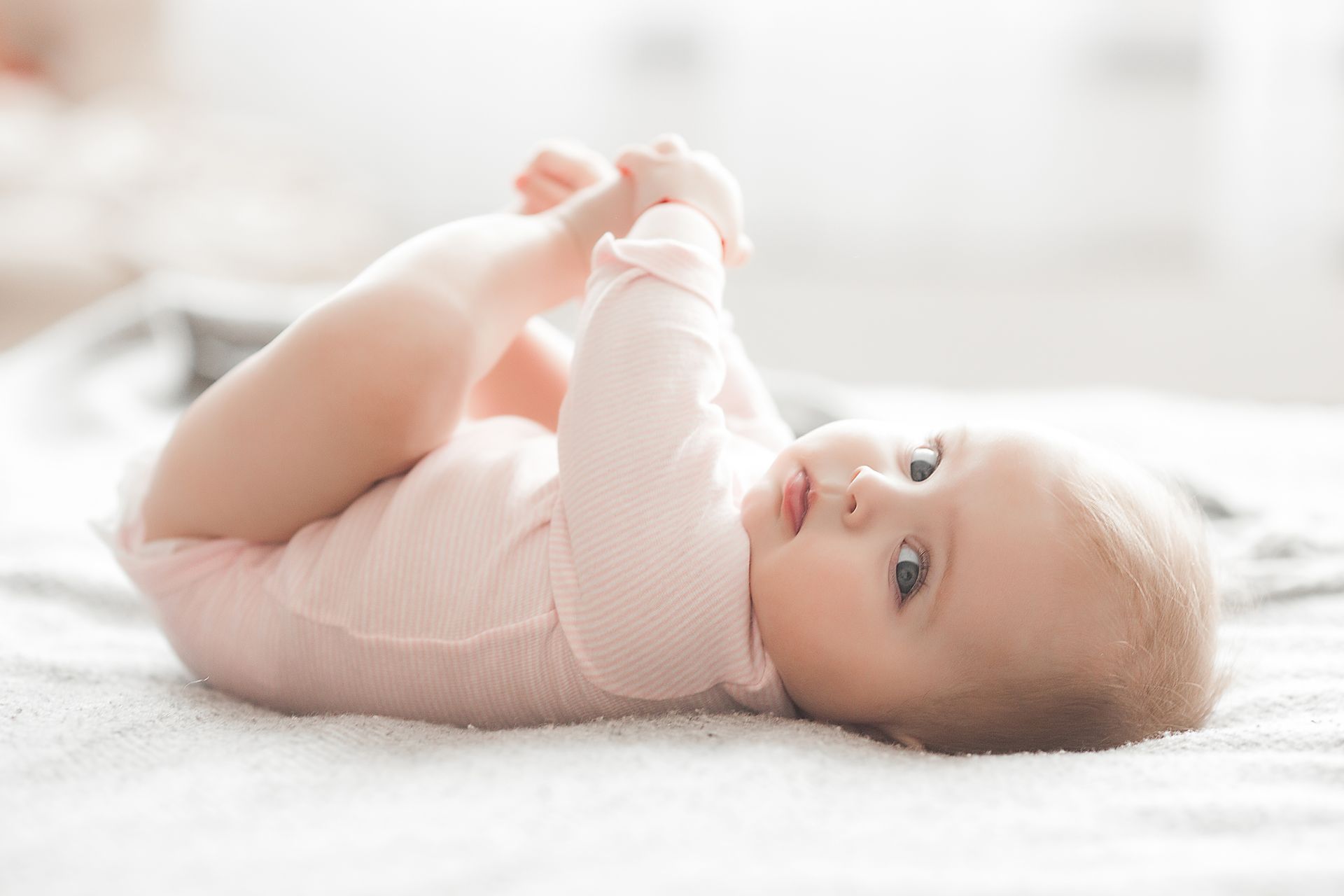 Un bébé sur le dos qui tient son pied gauche.