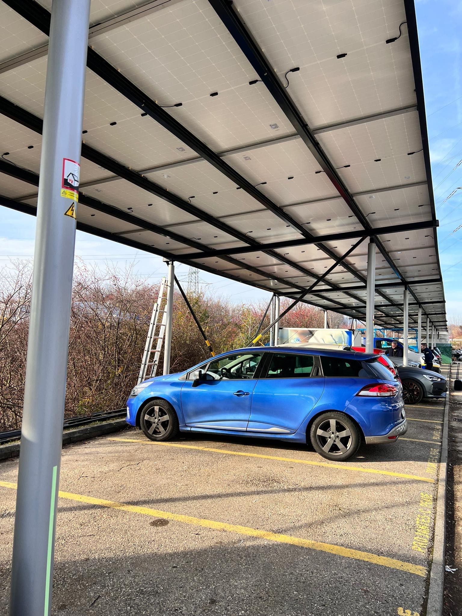 Une voiture bleue est garée sous un auvent dans un parking.