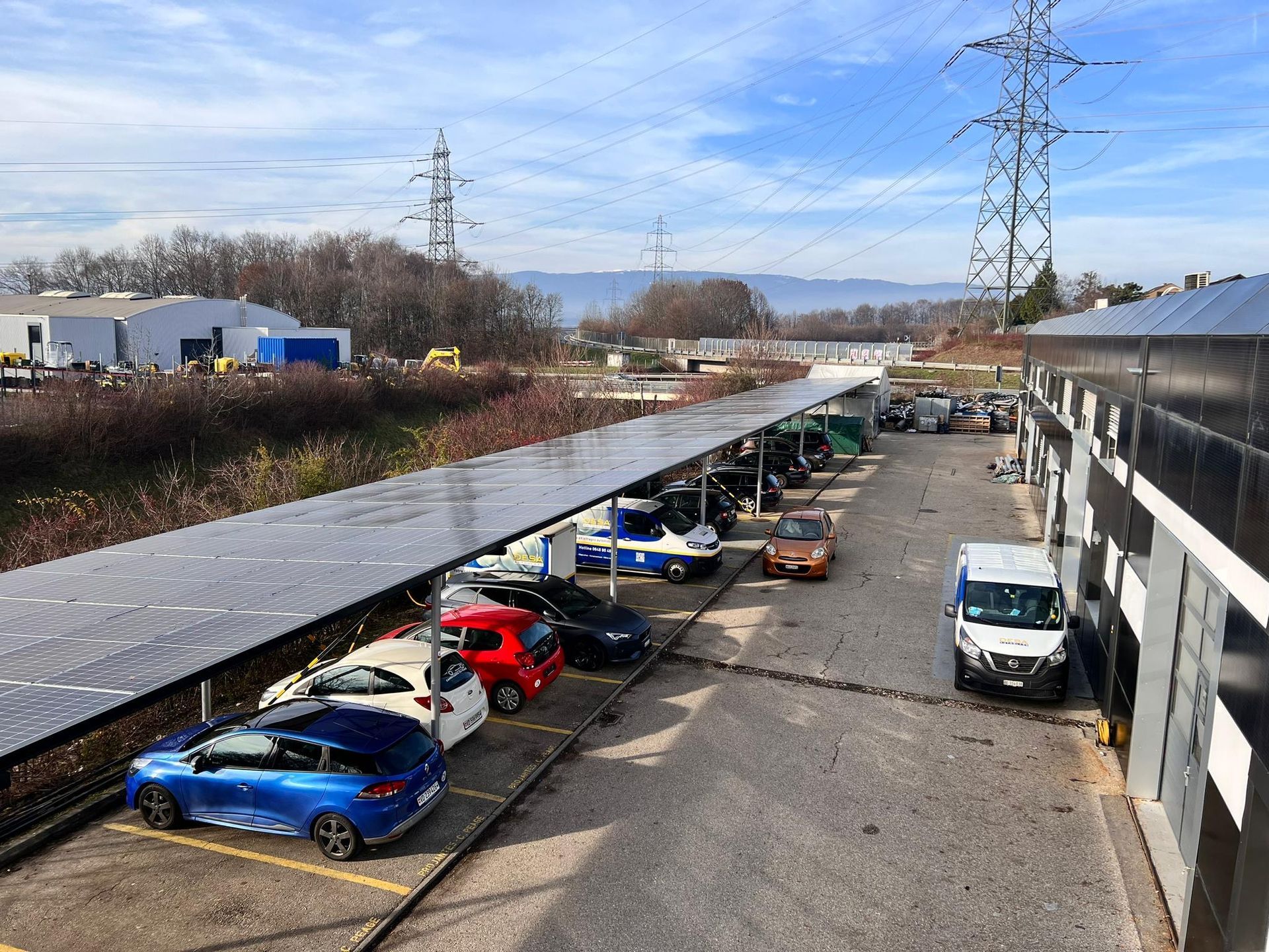 Beaucoup de voitures sont garées sous un auvent avec des panneaux solaires dans un parking.