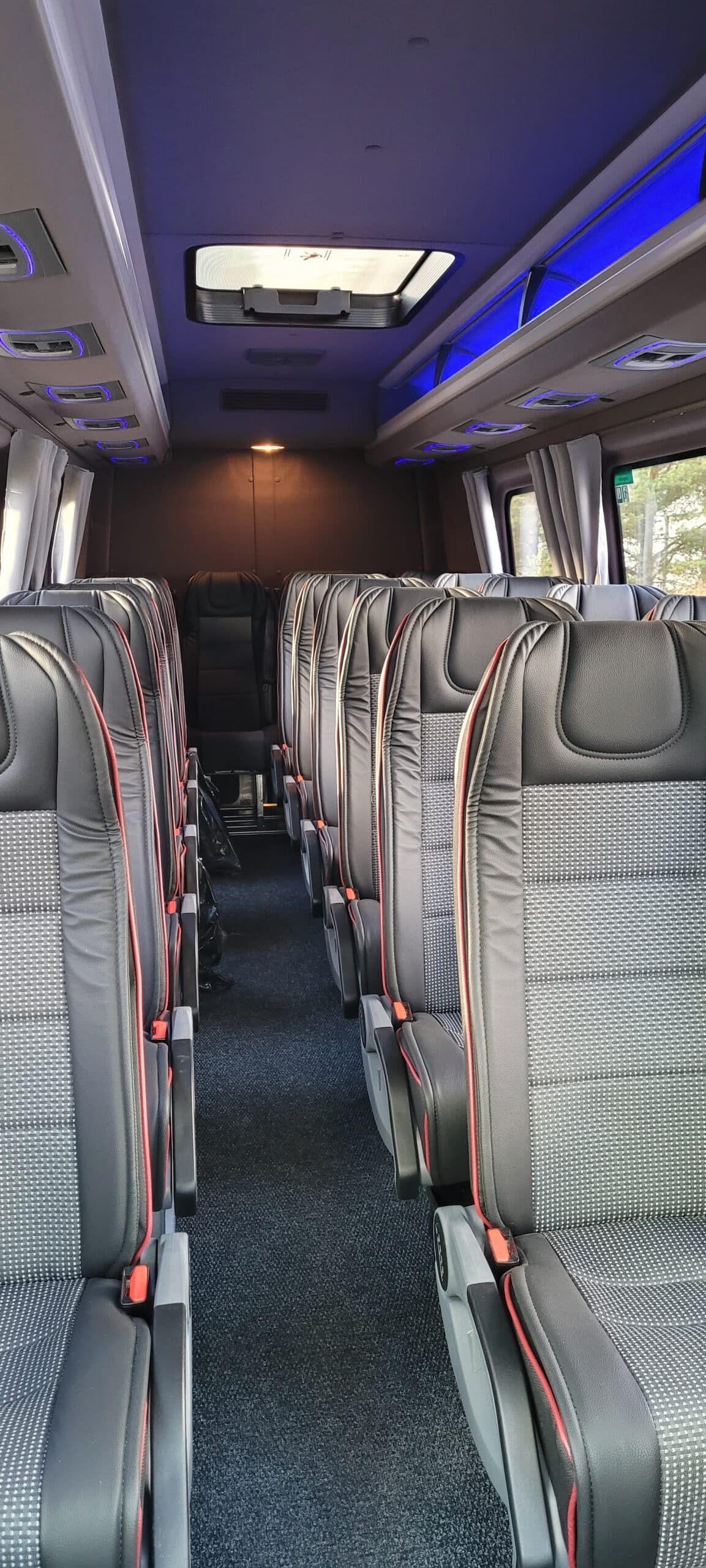 Tyhjä ylellisen kuljetusbussin sisätila, harmaat istuimet, sininen LED-valaistus ja näkymä käytävää pitkin