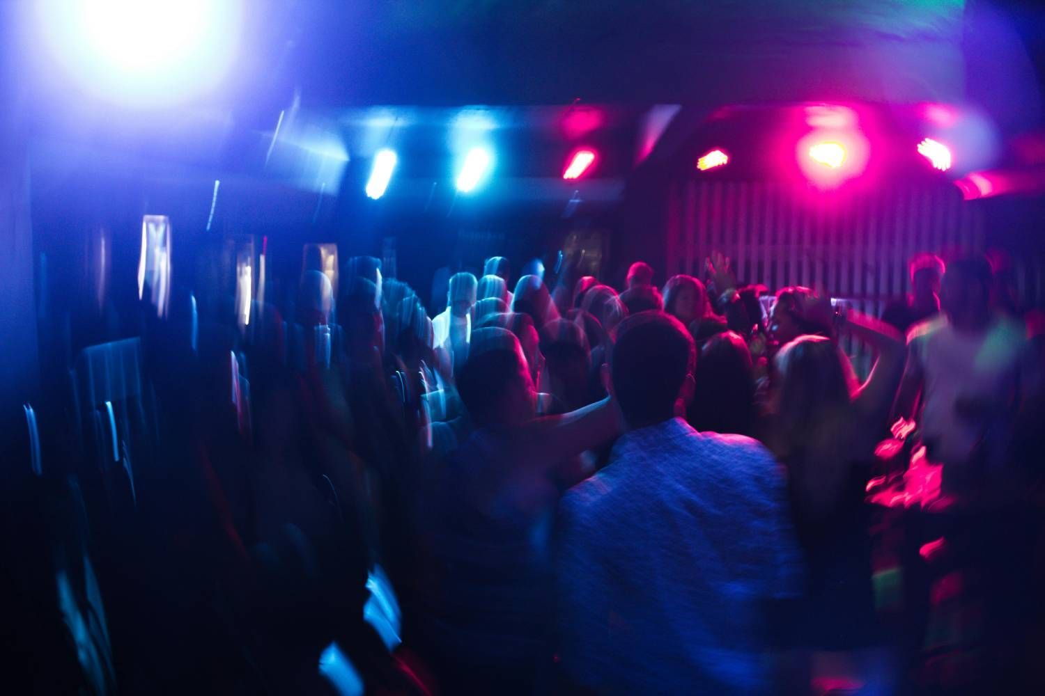 L'interno sfocato e scarsamente illuminato di una discoteca, con persone che ballano sotto luci di scena blu e rosa.