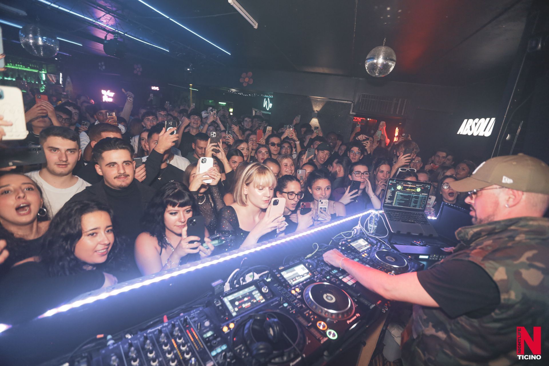 Una persona con indosso una maglietta di velluto rosso appoggia la mano su una palla da discoteca tra festoni dorati su una superficie bianca.