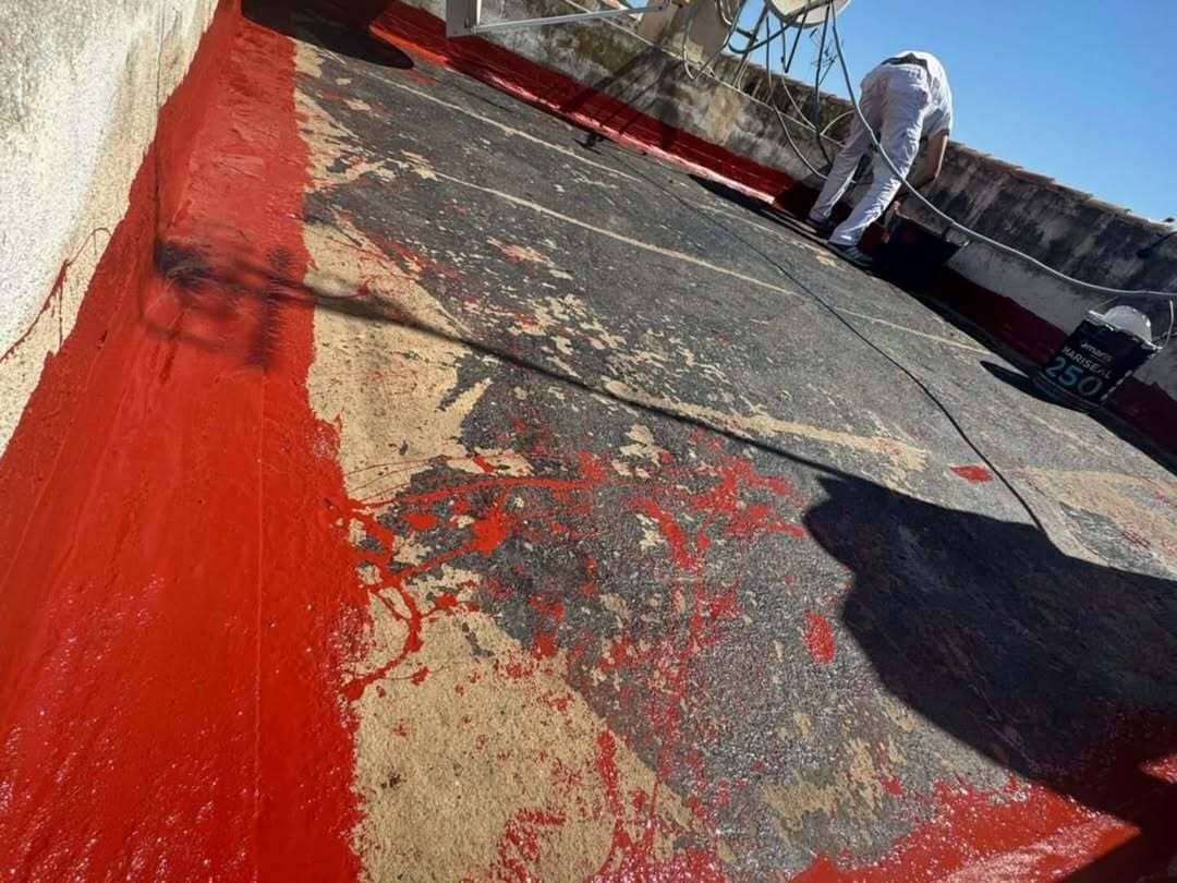 Una persona que lleva un guante amarillo está aplicando pintura negra a una superficie de hormigón con un pincel.