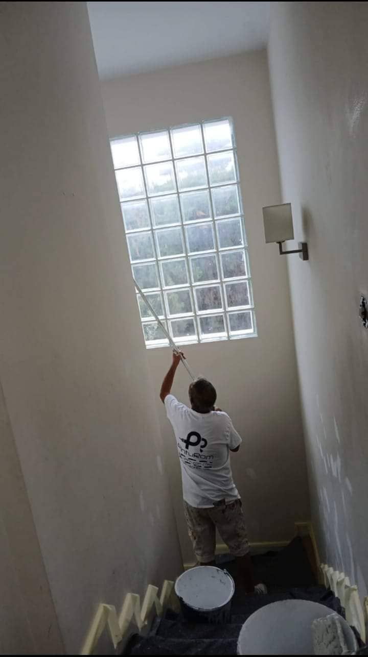 Un hombre está pintando una ventana de bloques de vidrio en un baño.