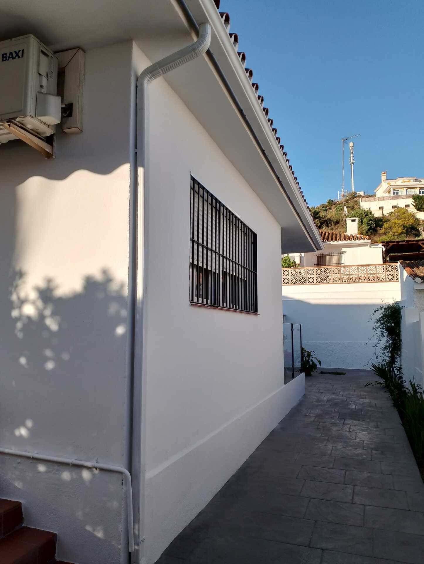 El costado de una casa blanca con un desagüe y una ventana.