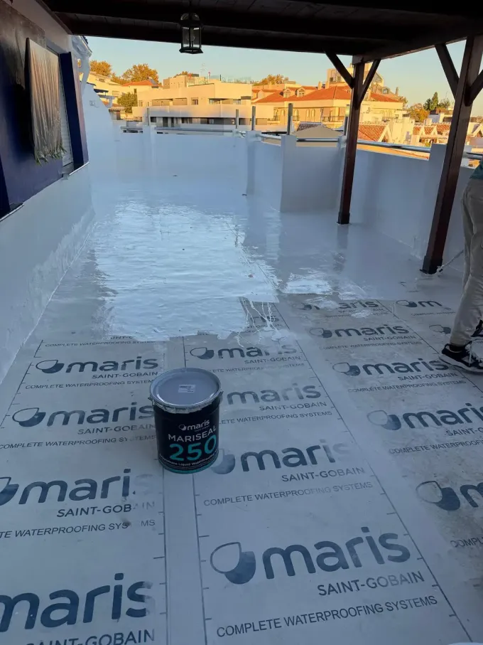 Un tejado impermeabilizado con pintura blanca. Se ven un cubo de pintura y un trabajador.