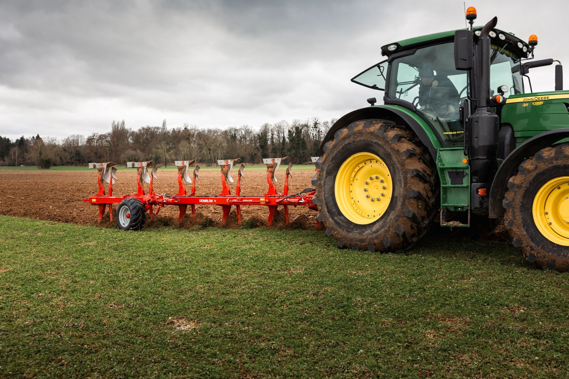 Un tracteur vert tirant une herse rouge