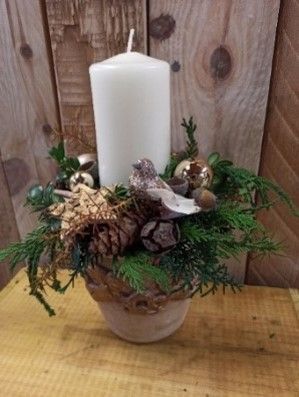 Eine weiße Kerze steht in einer Vase auf einem Holztisch.