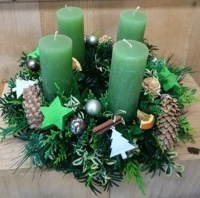 Ein Weihnachtskranz mit grünen Kerzen und Tannenzapfen auf einem Holztisch.