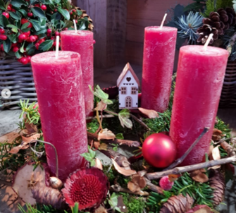 Ein Kranz mit vier rosa Kerzen und einem kleinen Haus