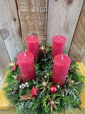 Ein Weihnachtskranz mit roten Kerzen und Grünpflanzen auf einem Holztisch.