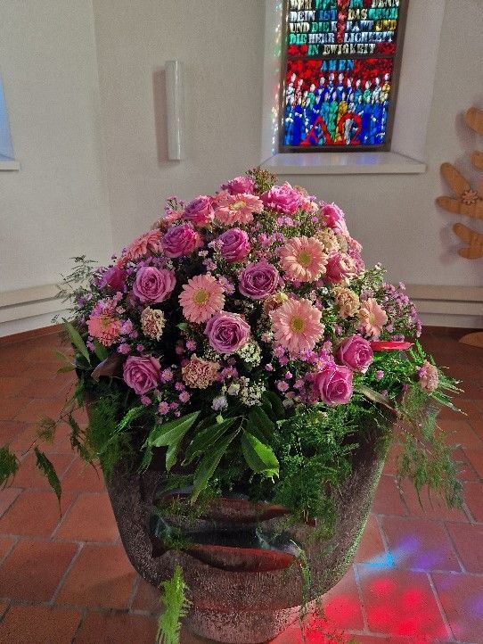 Eine Vase voller rosa Blumen in einer Kirche mit einem Buntglasfenster im Hintergrund.