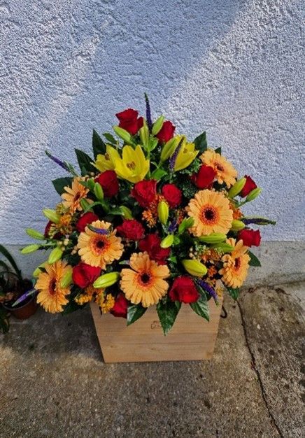 Auf einem Bürgersteig steht eine mit Blumen gefüllte Holzkiste.