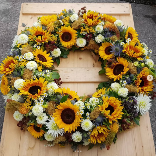 Ein Kranz aus Sonnenblumen und weißen Blumen auf einem Holztisch