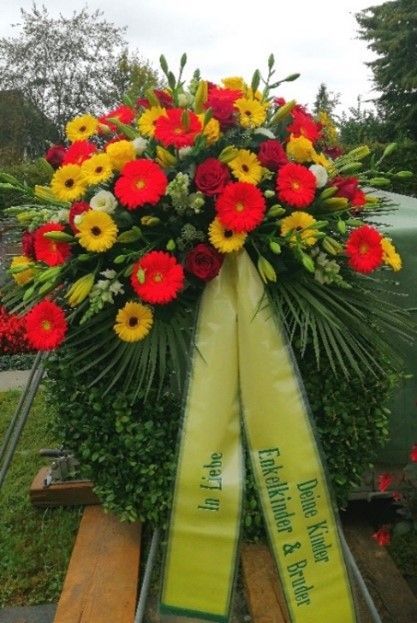 Ein Kranz aus roten und gelben Blumen mit einem gelben Band