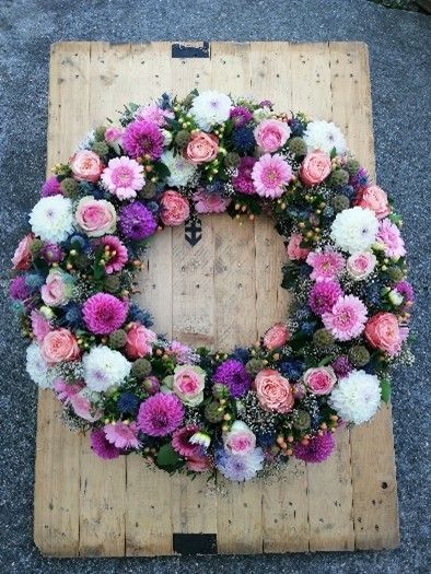 Auf einem Holztisch steht ein Kranz aus rosa und weißen Blumen.