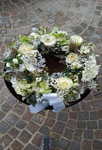 Eine Person hält einen Kranz aus weißen Blumen auf einem Tisch.