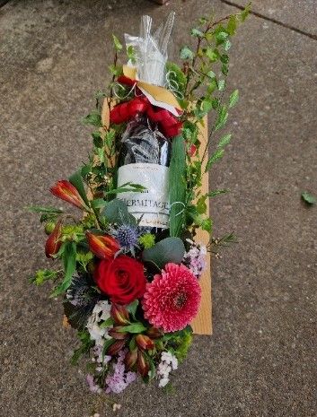 Eine Flasche Wein steht in einer Holzkiste, umgeben von Blumen.