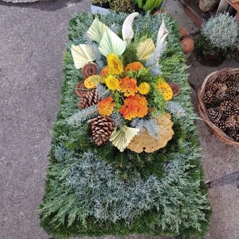 Auf dem Boden liegt ein Grab mit Blumen und Tannenzapfen.