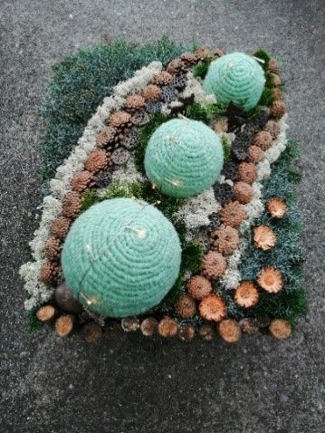 Auf einem Haufen Tannenzapfen liegt ein gehäkelter Ball.