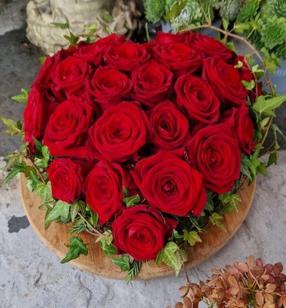 Ein herzförmiger Strauß roter Rosen auf einem Holzteller