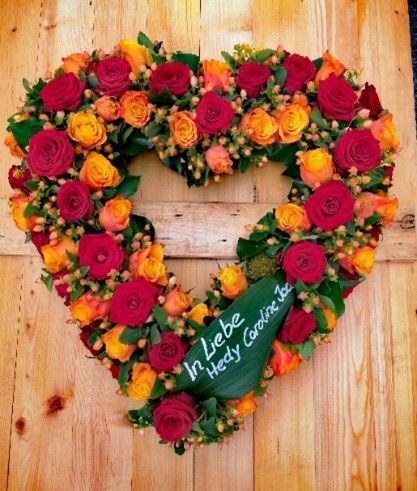 Ein herzförmiger Kranz aus roten und orangefarbenen Rosen mit den Worten „in Liebe Heidi“ darauf geschrieben