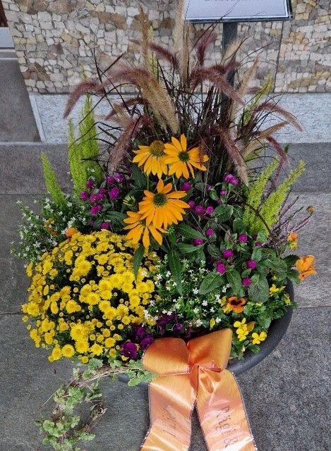 Eine Vase gefüllt mit gelben und violetten Blumen mit einer orangefarbenen Schleife