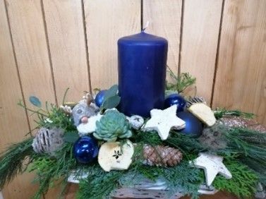 Auf einem Holztisch ist eine blaue Kerze von Blumen und Dekorationen umgeben.