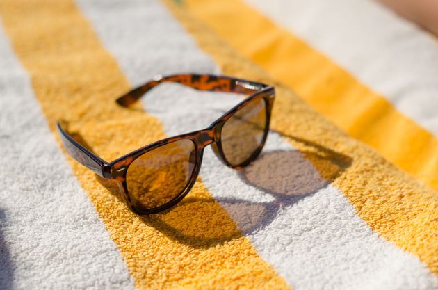 Gafas de sol marrones sobre una toalla a rayas amarillas y blancas bajo la luz del sol.