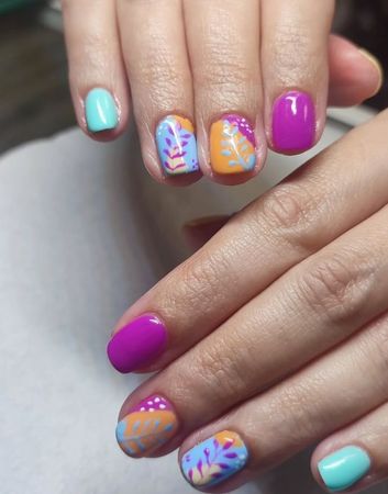 Un primer plano de las uñas de una mujer con diseños en tonos morados, azules y naranjas.