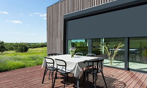 Vue en contre-plongée d'un immeuble d'appartements moderne avec une façade blanche, un étage penthouse gris et des volets extérieurs.