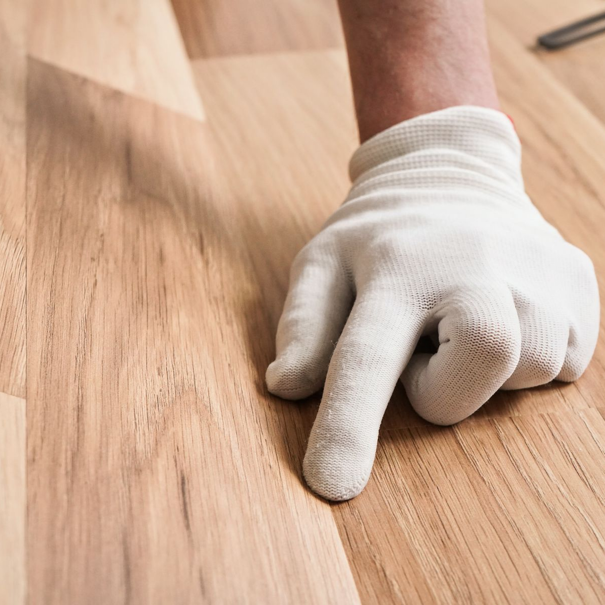 Main gantée pointant du doigt le parquet nouvellement installé.
