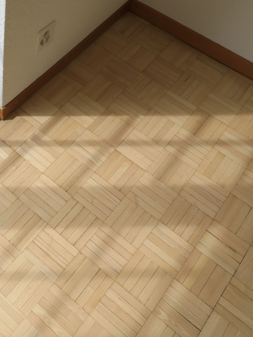 Un parquet clair dans un coin de pièce, avec des ombres projetées par une fenêtre.