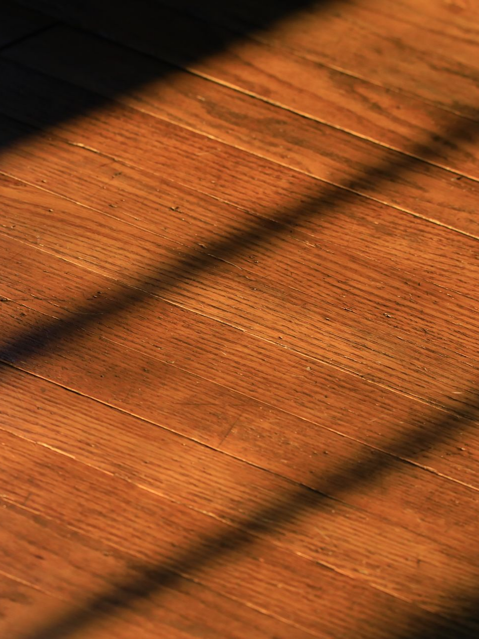 Plancher en bois, brun chaud, traversé par une ombre en diagonale.